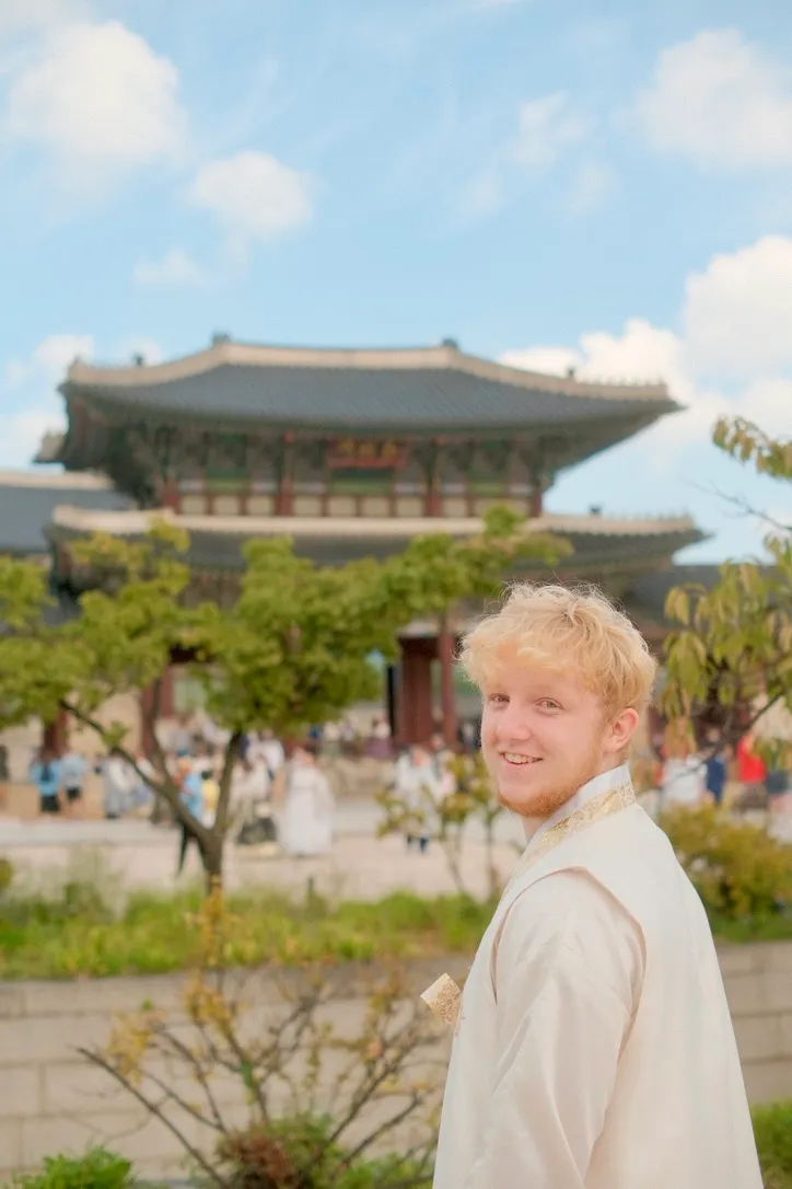 Daniel Pfurner, lachend, in einem hellen Hanbok vor dem Gyeongbokgung-Palast in Seoul